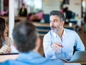 Three work colleagues talking together at office desk in coworking office