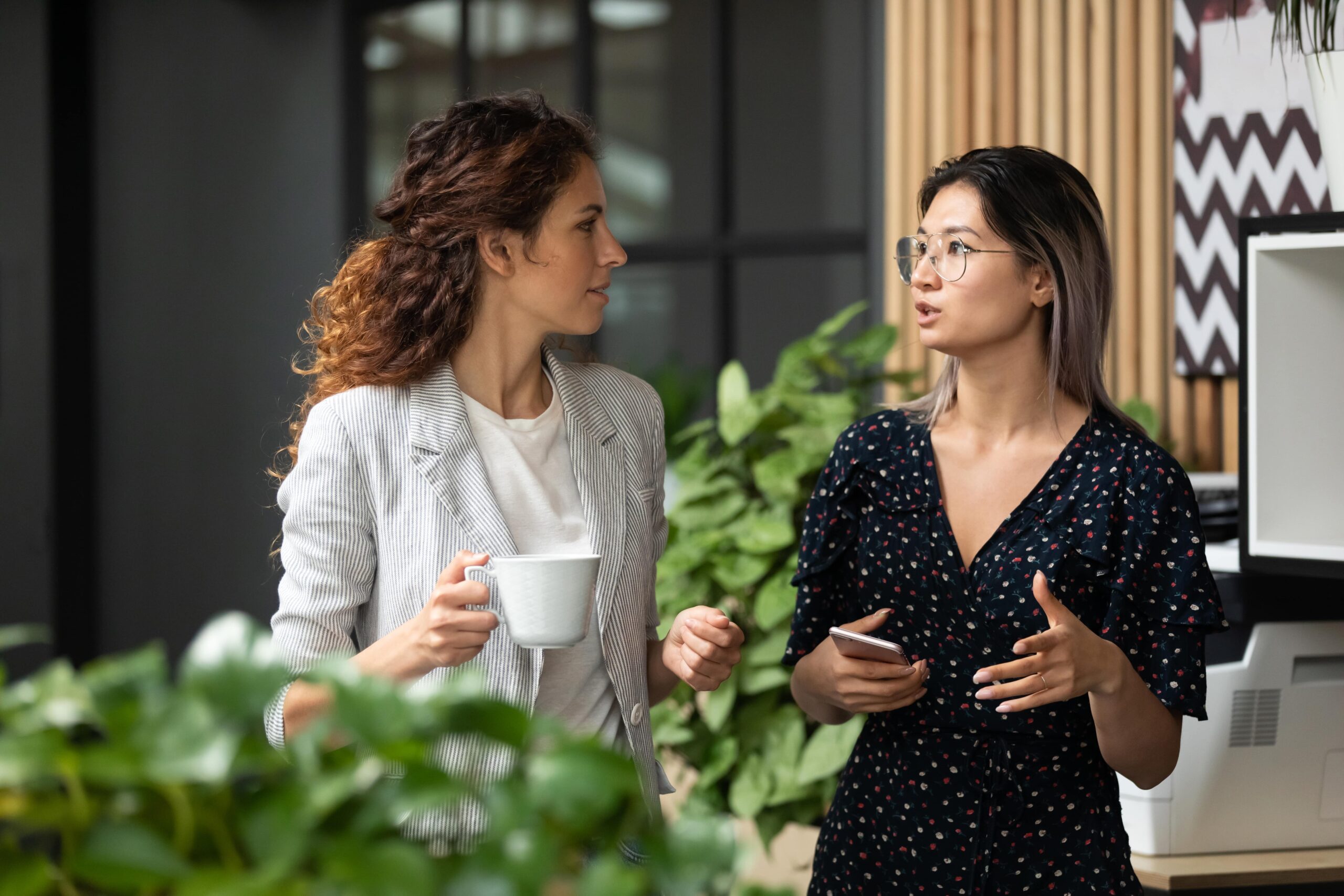 Two professional women walk side by side in an office.
