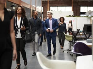 Businesspeople Arriving For Work In Busy Modern Open Plan Office
