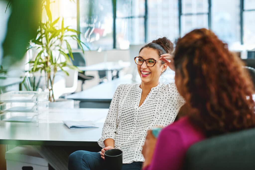 Female professionals sit in an office environment, smiling