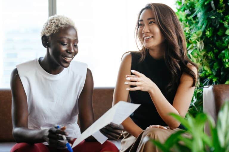 Two female colleagues sit side by side reviewing paperwork