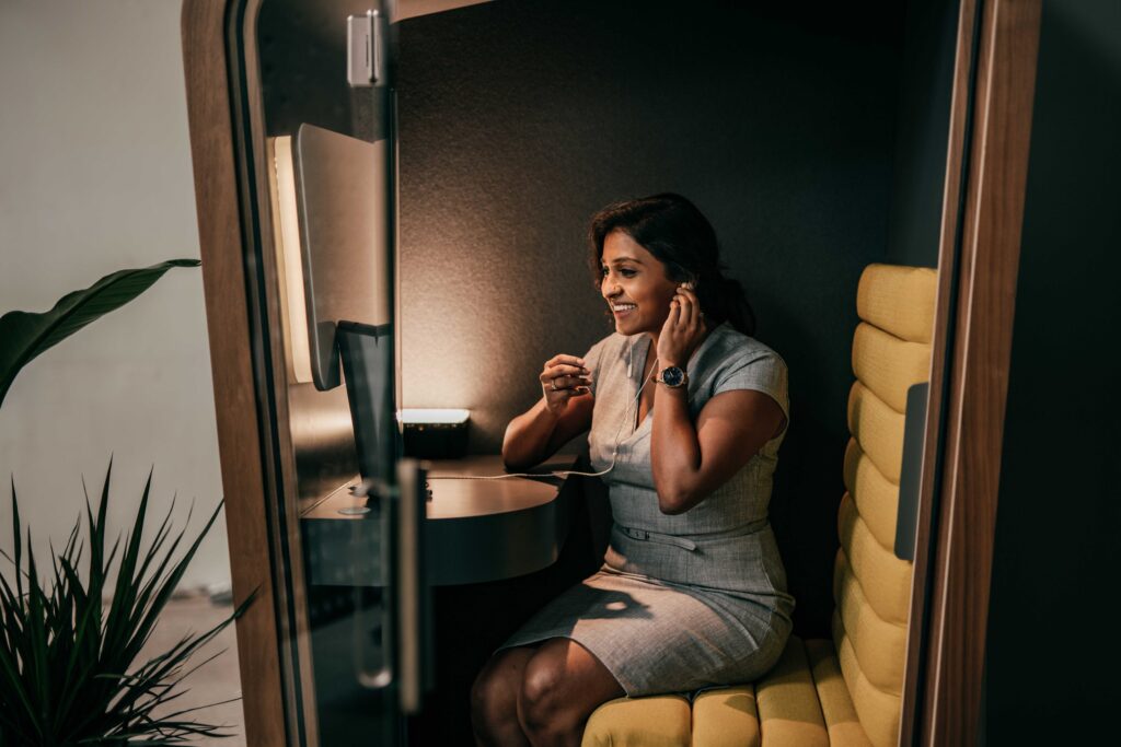 A smartly dressed lady sits in a work meeting booth on her phone, mid conversation