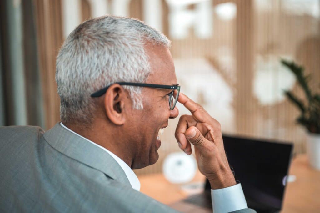 A gentleman in a suit, pushes his glasses whilst sat in his work office at his laptop