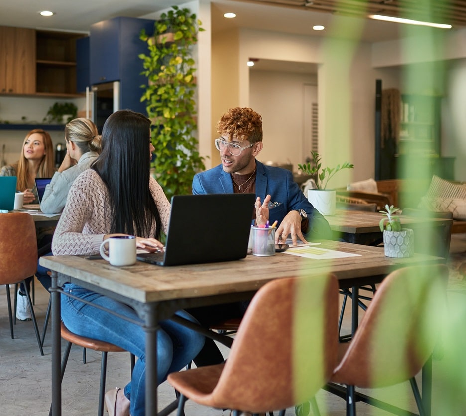 Focus on two young professionals with a laptop, sitting in a cafeteria environment