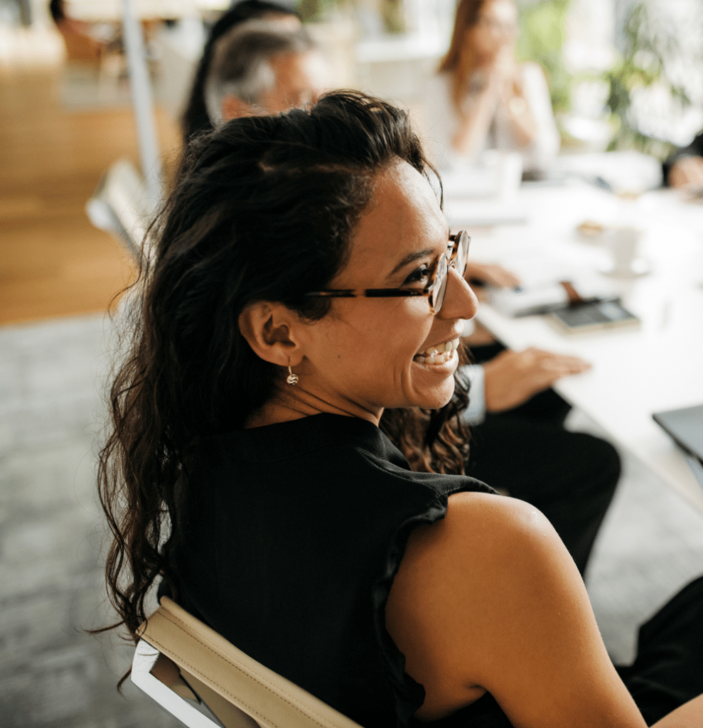 A woman sits at a meeting room table, smiling
