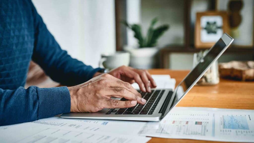 A gentleman types at a desk on his laptop at home