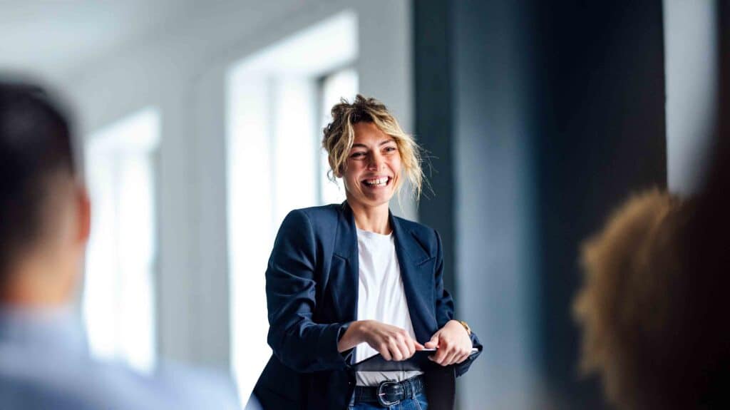 A lady stands in a suit smiling, holding a tablet device