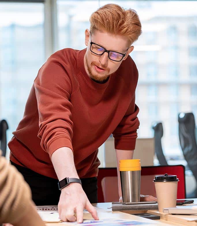 A man stands over a desk, he is wearing glasses