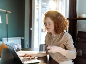 Young woman working at home. She is sitting at the desk in the home office and looking at a laptop